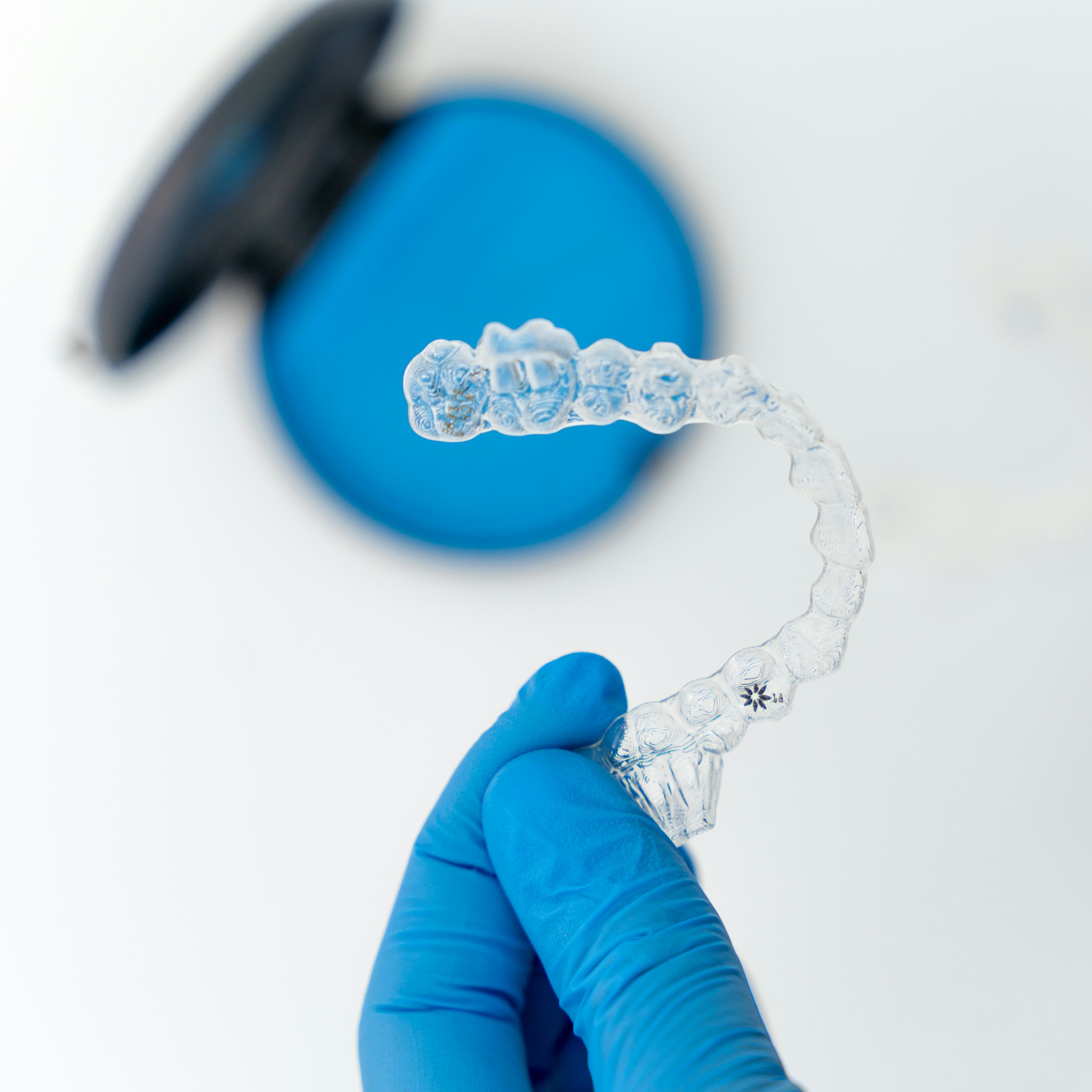 Behandschuhte Hand hält einen transparenten Invisalign® Aligner mit Aufbewahrungsbox - Zahnarztpraxis Dr. Salem in Krefeld-Traar